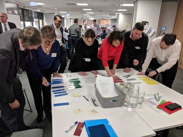 A group of people stand around a table ranking information on cards.